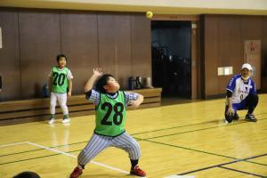 バッターボックスから足を踏み出してゴムボールを打つ小学生